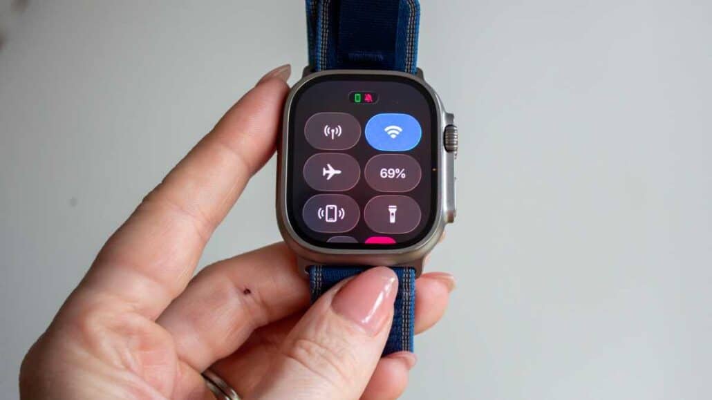 Close-up of a smartwatch on a blue strap being held by fingers, showing a control panel with icons and battery 69%.