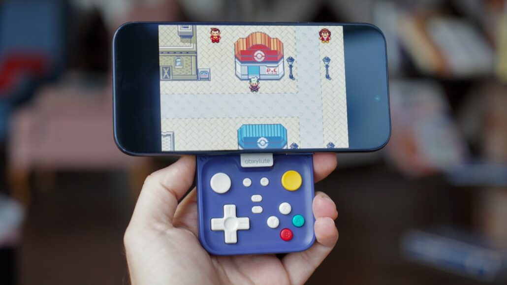 Blue clip-on handheld gamepad attached to a smartphone displaying a pixel-art town scene from a retro game.