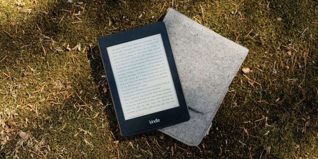Kindle e-reader resting on a flat gray stone on mossy ground outdoors.