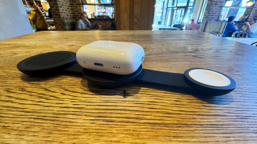 White wireless earbuds case resting on a circular charger on a wooden cafe table.