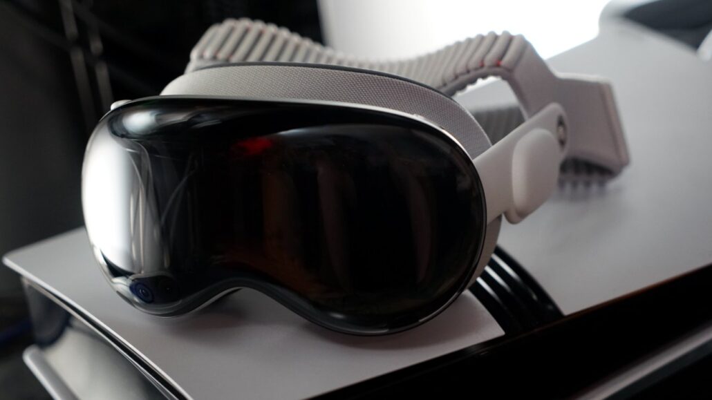 White ski goggles with a dark-tinted lens and beige adjustable strap resting on a silver laptop surface.”] ,