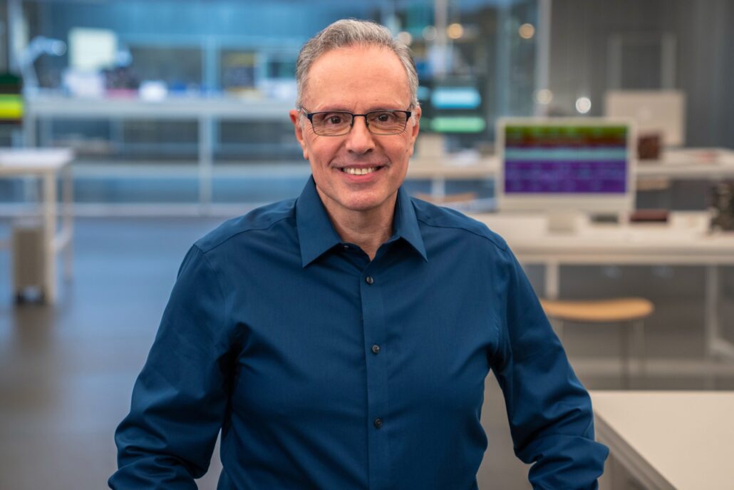 Smiling man with glasses in a blue shirt posing in a modern lab or office setting
