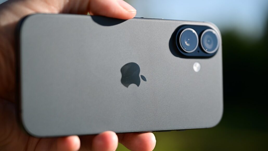 Rear view of a gray iPhone with a dual-camera system held in a hand, outdoor background.