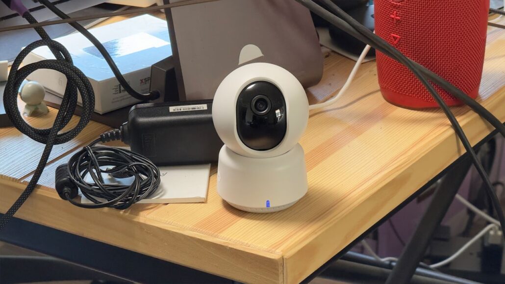 White dome security camera on a cluttered wooden desk with cables and a red speaker nearby