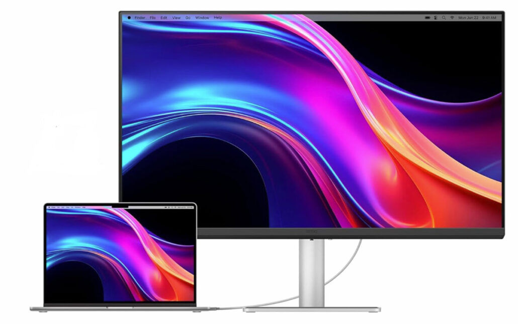 Desktop monitor on a silver stand with a laptop in front, both displaying the same vivid abstract wallpaper in blue, purple, and pink hues.