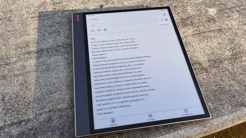 Tablet on a stone surface displaying a dictionary entry for the word 'Iron' with full definition visible on screen.