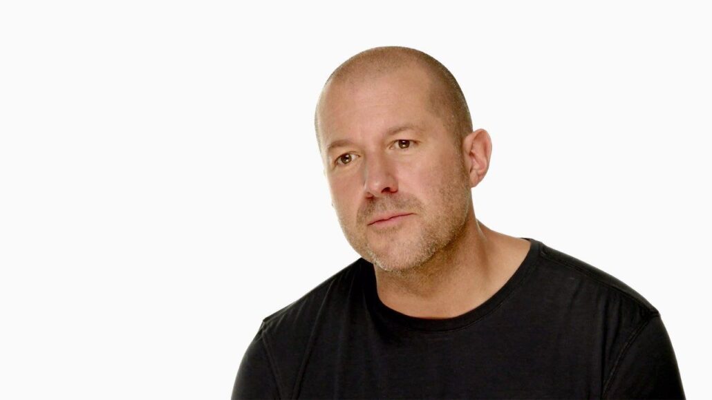 Close-up portrait of a bald man with light stubble wearing a black T-shirt against a white background in a studio setting.