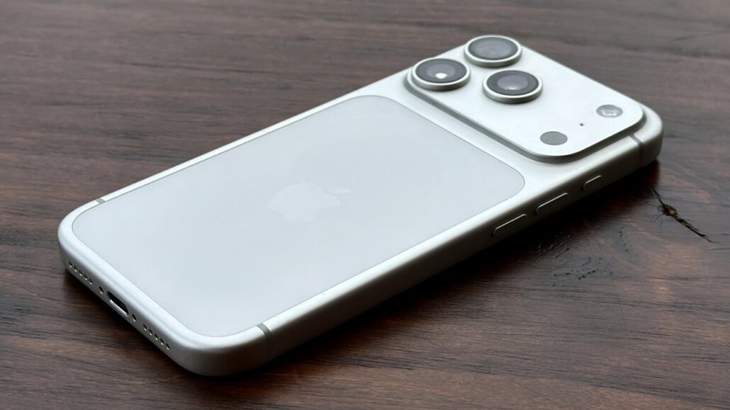Silver iPhone with a triple-camera setup lying on a dark wooden surface, showing the back and Apple logo in the center of the glass panel.