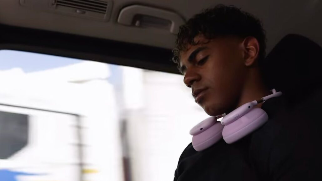 Young man wearing pink over-ear headphones around his neck, looking down while seated in a car interior