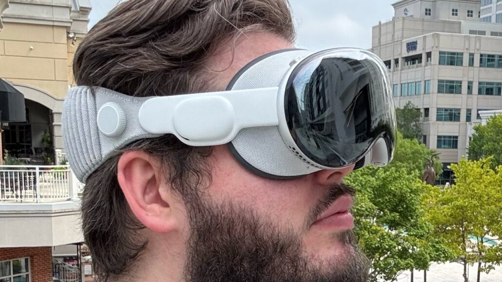 Slimmer lighter Apple Vision Pro is at least two years away - Dans Tutorials - Dans Tutorials Man with a white VR headset and strap around his head, looking to the right in an outdoor urban setting.