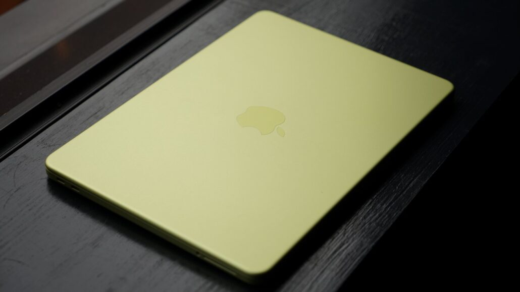 Bright yellow-green laptop closed with an Apple logo on a dark wooden surface.