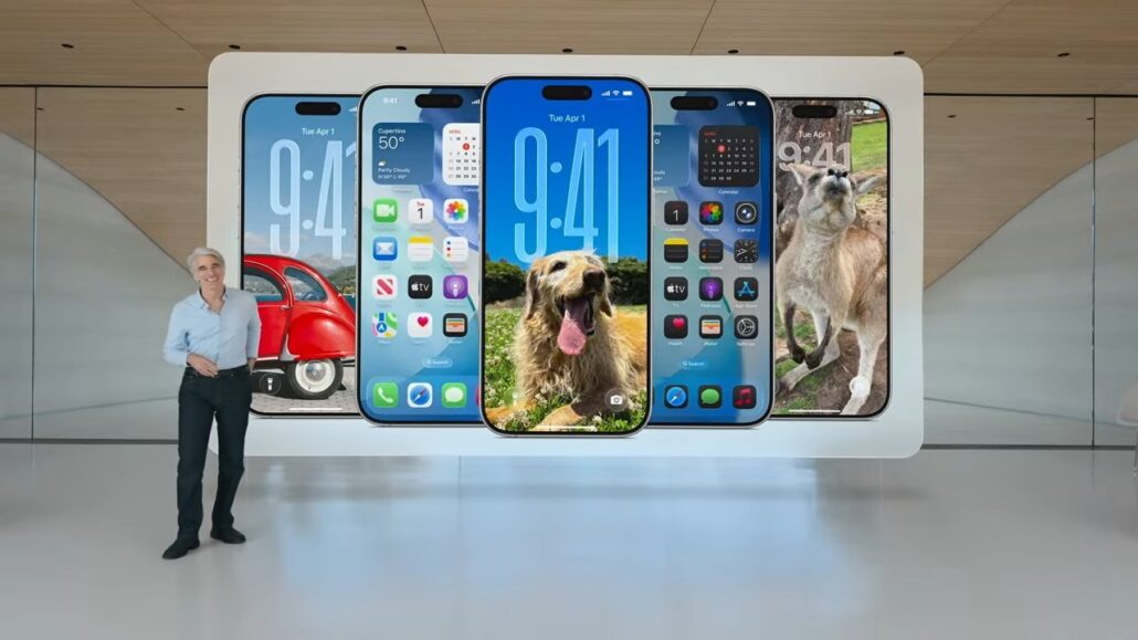 Surprising nobody Apples already working on iOS 28 macOS 28 - Dans Tutorials - Dans Tutorials Man stands beside a large wall display showing several iPhone models with different home screens and dog wallpapers in a modern showroom setting.