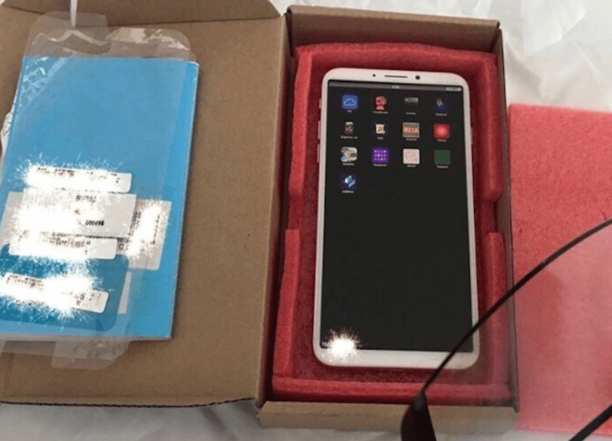 New white tablet/smartphone in red foam insert inside an open box, with blue packaged item beside it on the left.