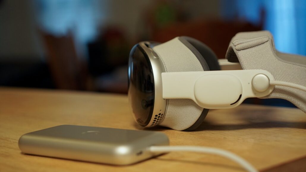 White over-ear VR headset with cushioned ear cups resting on a table, connected to a slim silver device via a cable