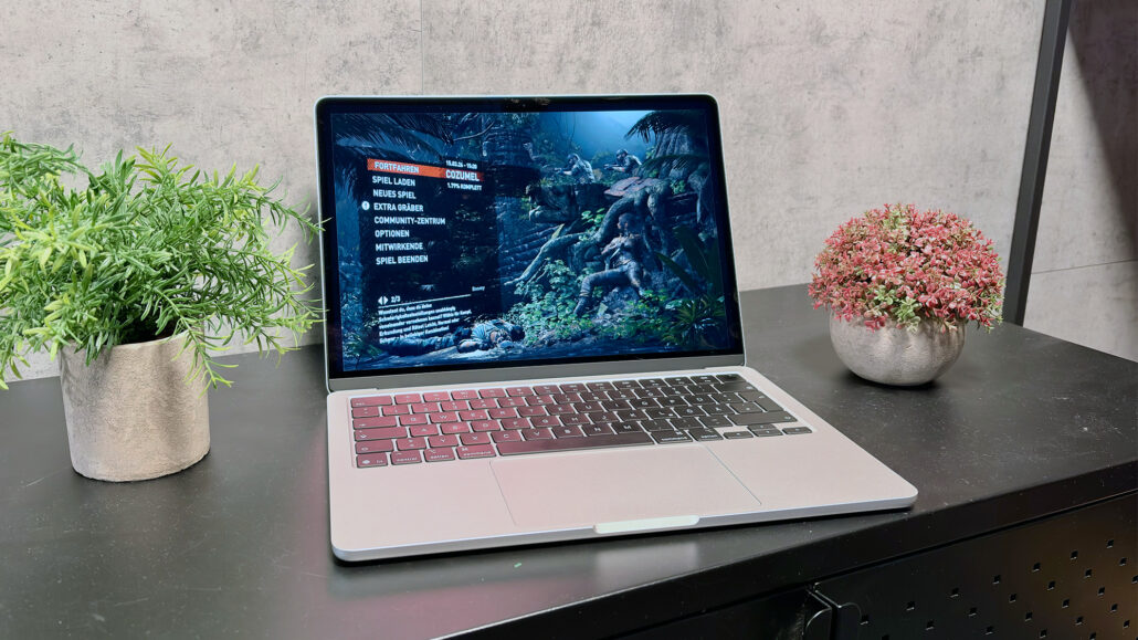 Laptop on a black desk showing a jungle-themed game menu, flanked by green and pink potted plants on either side.