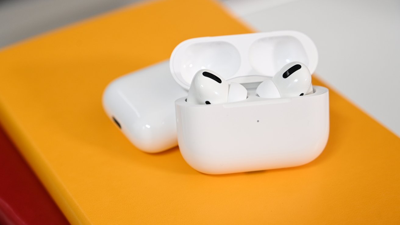 AirPods Pro Beats Studio Buds move to new firmware versions - Dans Tutorials - Dans Tutorials White wireless earbuds in their charging case resting on an orange surface.
