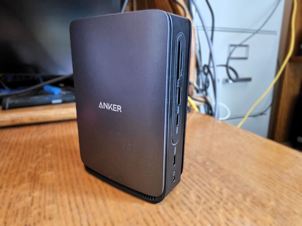 Close-up of a black Anker docking hub with side USB ports on a wooden desk.