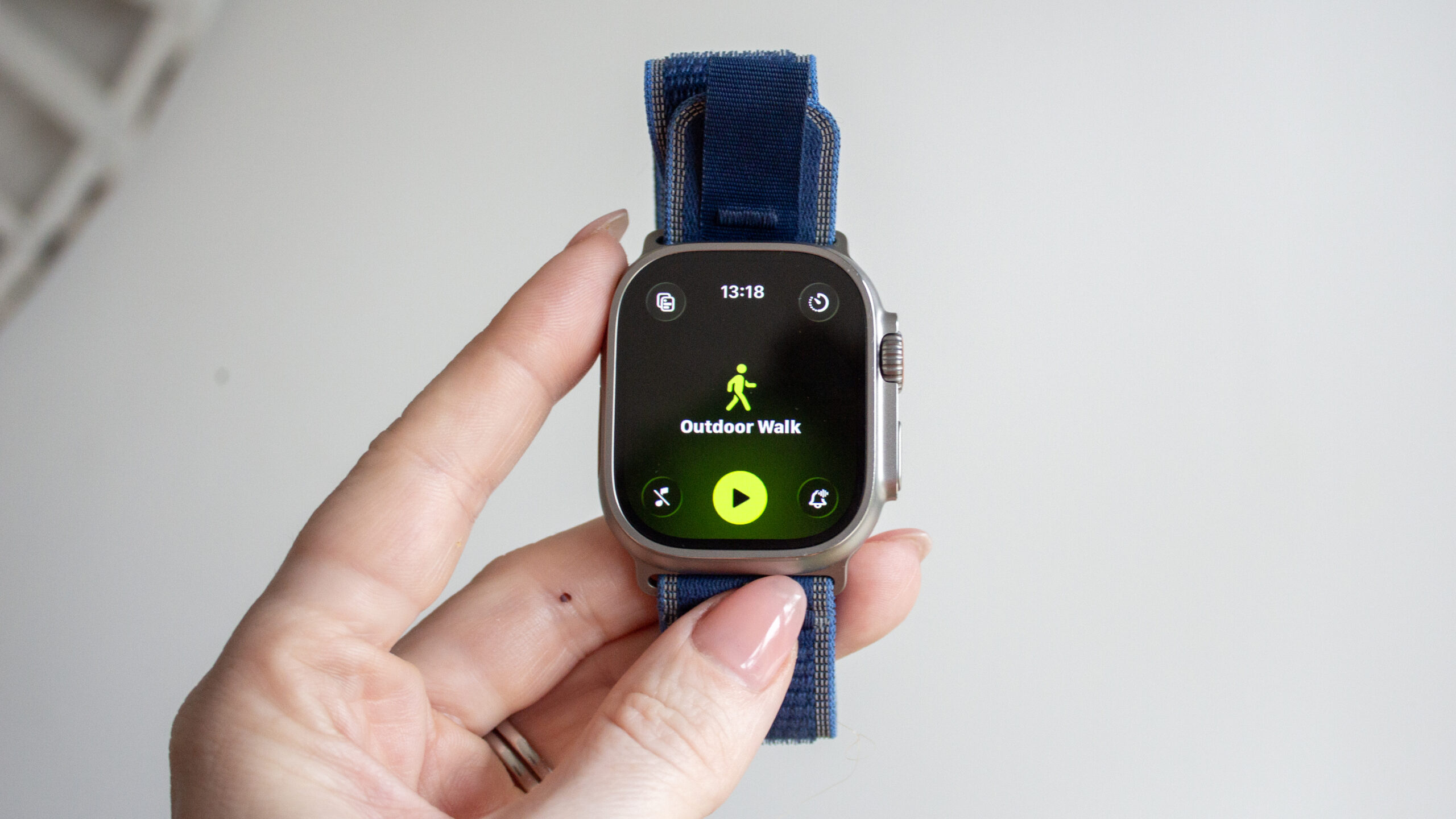 Apple Watch Ultra 3 gets a 0 price cut ahead of Prime Day - Dans Tutorials - Dans Tutorials Smartwatch with blue strap held by fingers, showing an 'Outdoor Walk' workout on the screen with a walking icon and play button.