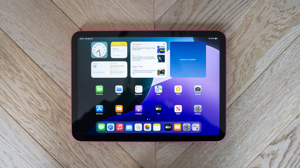 Pink-edged tablet showing a home screen with app icons on a wooden floor.