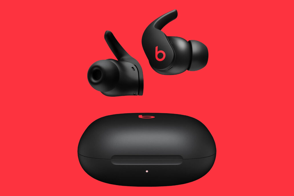Beats wireless earbuds with their charging case on a red background, showcasing the black, in-ear design.