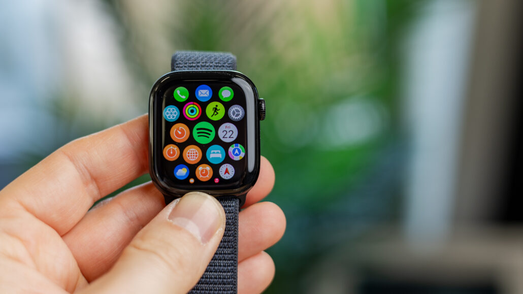 Close-up of a smartwatch held by fingers, displaying a grid of colorful app icons on its screen.