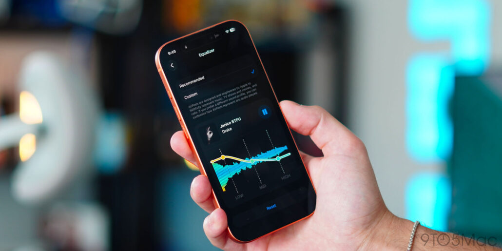 Hand holding a smartphone showing an equalizer screen with waveform and settings in focus.