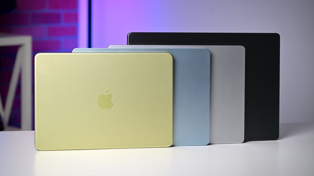 Five closed laptops in gold, light blue, gray, silver, and black arranged in a staggered fan on a white desk, Apple logo visible on the gold one