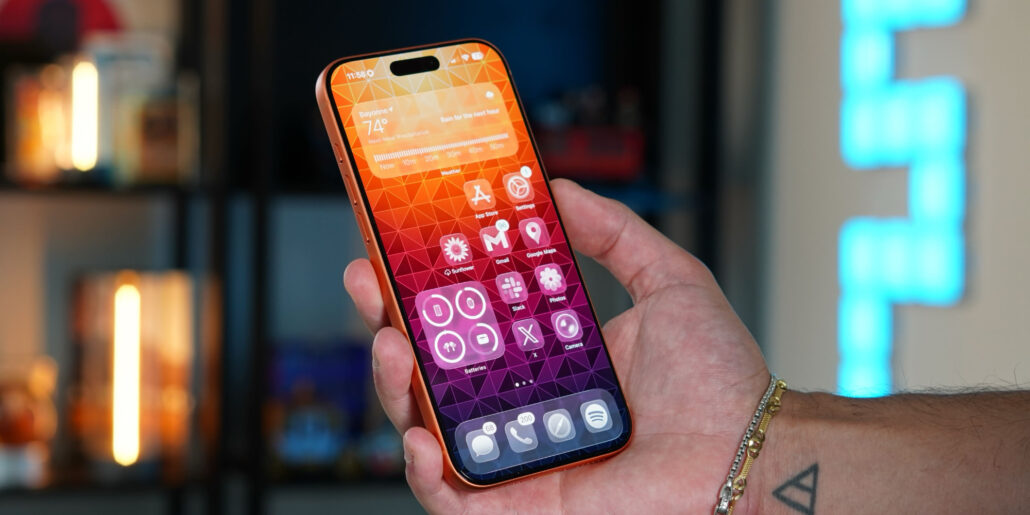 iOS 27 Seven new iPhone features are coming soon - Dans Tutorials - Dans Tutorials Hand holds a colorful iPhone with geometric wallpaper and app icons visible on screen.
