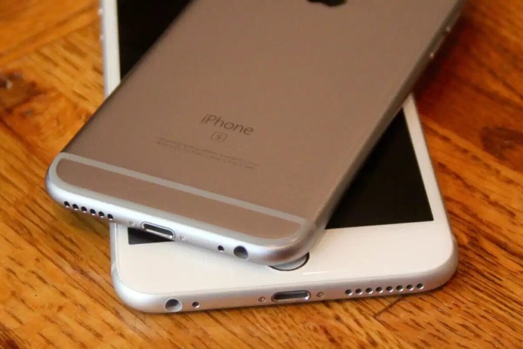 Two iPhones stacked on a wooden table, one face-down showing the back with Apple logo in view.