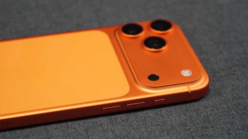 Orange smartphone back with three camera lenses on a gray fabric surface, side buttons visible.