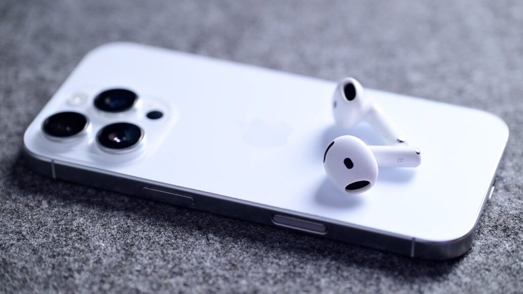 White smartphone with wireless earbuds resting on its back on a gray textured surface, close-up view.