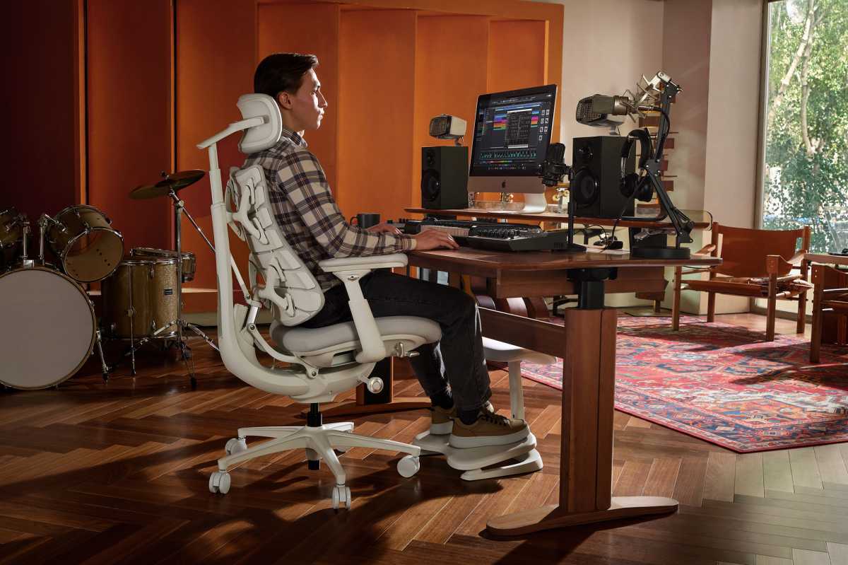 LiberNovo Maxis The ergonomic chair redesigned for the bodies that design everything else - Dans Tutorials - Dans Tutorials Person seated at a wooden desk in a home recording studio, editing on a monitor with studio speakers and microphones nearby.