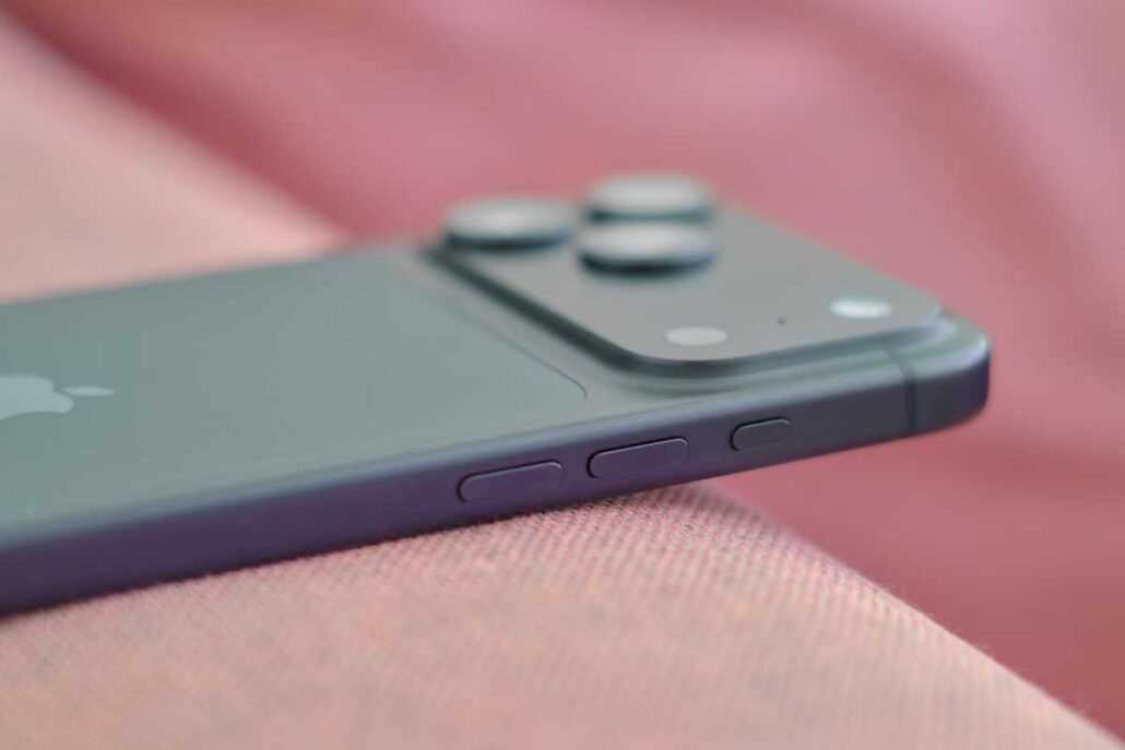 Close-up of a dark gray iPhone with its dual-camera module and side buttons on pink fabric.