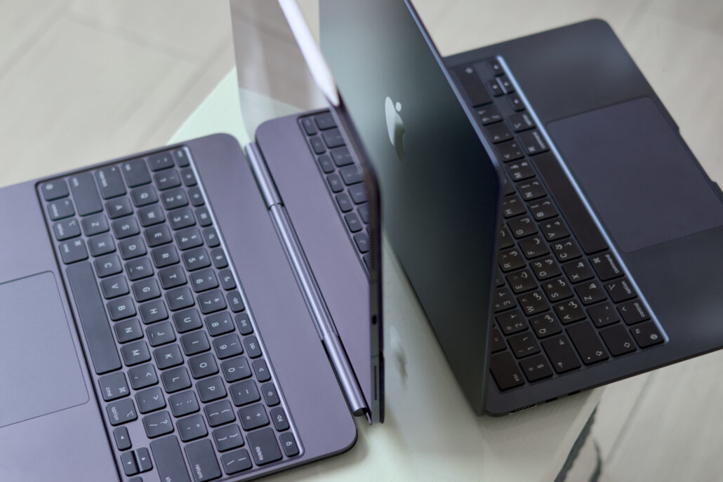 Three open laptops arranged on a light table, angled toward the camera with visible keyboards and one lid showing an Apple logo