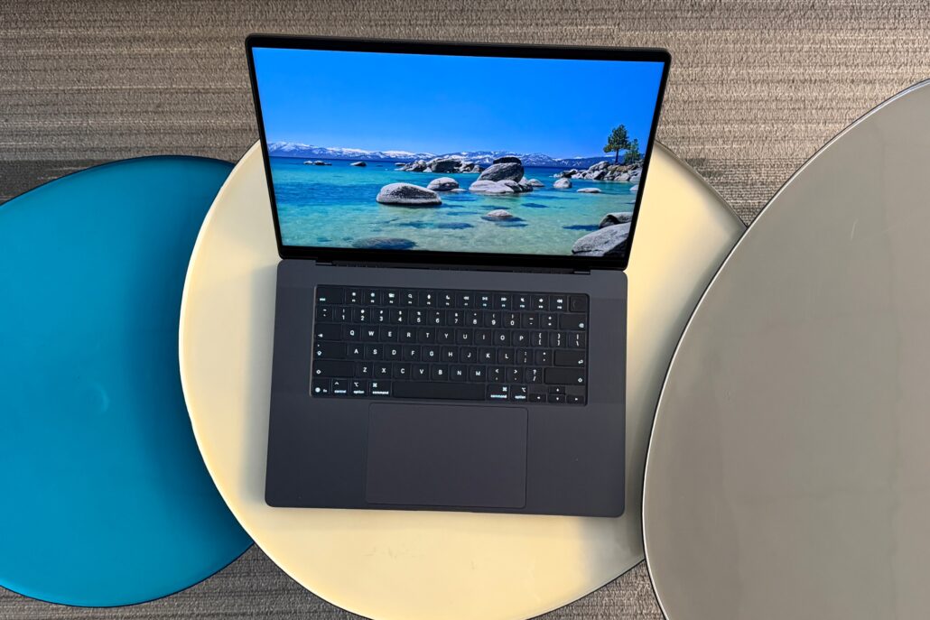 Open laptop placed on overlapping round surfboards; screen shows a tropical beach with turquoise water and rocks under a blue sky.