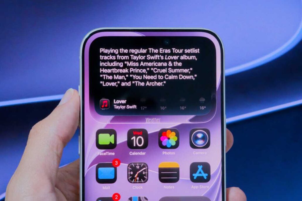 Close-up of an iPhone held in a hand, showing a large text-rich widget at the top and app icons on a purple wallpaper below.