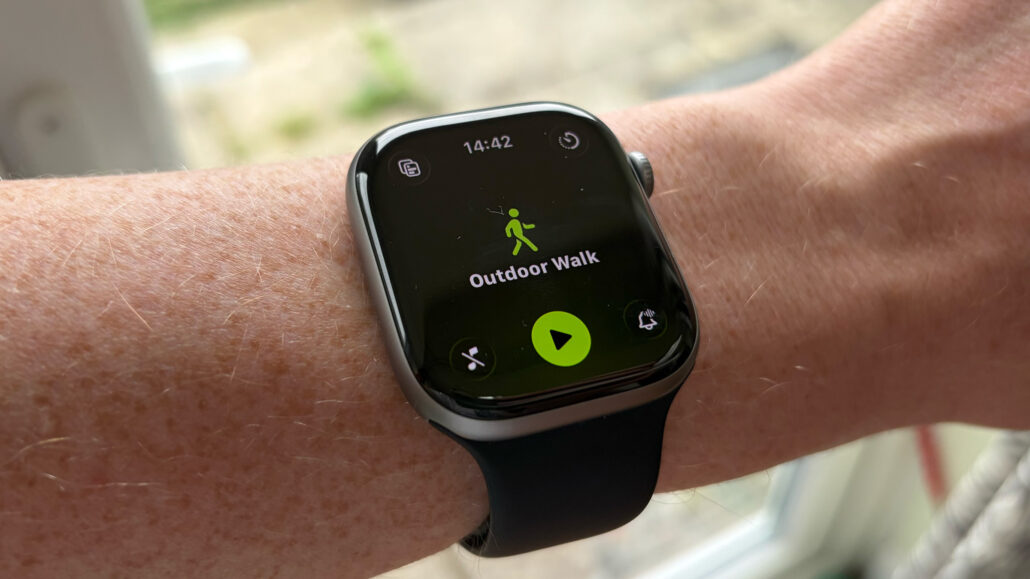 Smartwatch on a wrist displaying Outdoor Walk mode with a green start button and walking icon outdoors