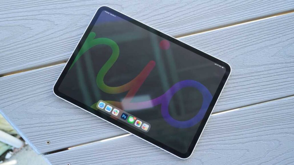 Tablet with a colorful abstract wallpaper on a blue wooden table surface, dock visible at bottom edge of screen