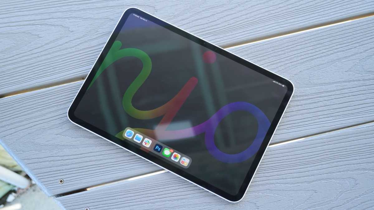 Tablet with a colorful abstract wallpaper on a blue wooden table surface, dock visible at bottom edge of screen