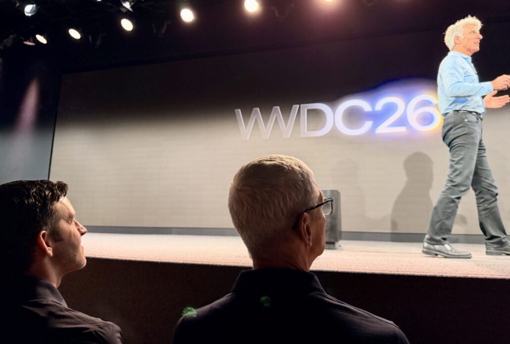 WWDC 2026 Emptying the notebook about AI bug fixes and more - Dans Tutorials - Dans Tutorials Speaker delivering a talk on stage at WDC26, with two audience members in the foreground watching.