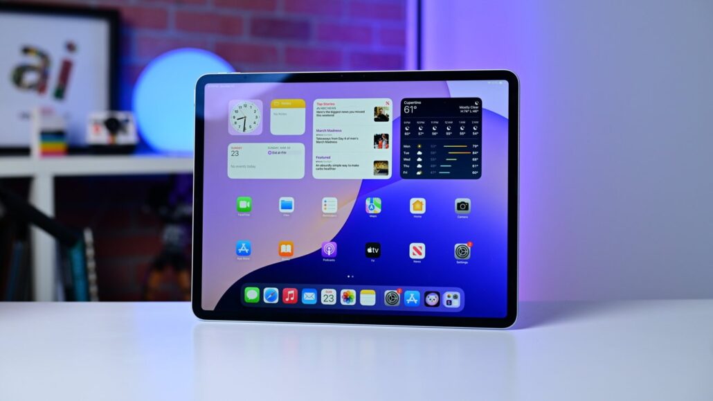 You can buy unlimited ATT data for your iPad for a day - Dans Tutorials - Dans Tutorials Tablet on a white table displaying iPadOS home screen with widgets and app icons against a blue-purple background for context/scene.